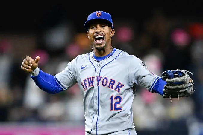 Francisco Lindor in a New York Mets road uniform, arms outstretched, celebrating on the field.